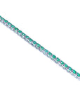 The side view of a white gold tennis bracelet with round cut emeralds on a white background.