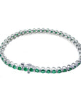 The underside view of a white gold tennis bracelet with emeralds on a white background.
