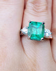 Emerald three stone ring with diamond accents on a finger.