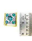 A yellow and white gold emerald cufflink next to a ruler for scale on a white background