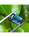 5.05 ct GIA certified deep blue-green emerald cut sapphire held by tweezers.