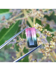 Emerald cut 6.11 ct natural loose watermelon tourmaline, bluish-green to red-orange, held by tweezers.