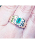 Men's gold ring with a square natural emerald worn between fingers.