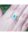 Men's 14K yellow gold ring with a rectangular Muzo emerald and diamond halo, worn on a hand.