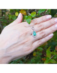 Hand displaying a white gold pendant with a natural emerald against a natural background.