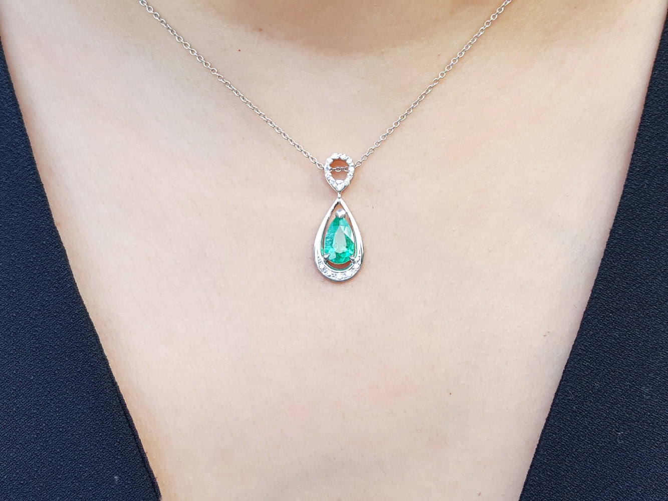 Emerald teardrop pendant necklace on a person wearing a dark blue top.