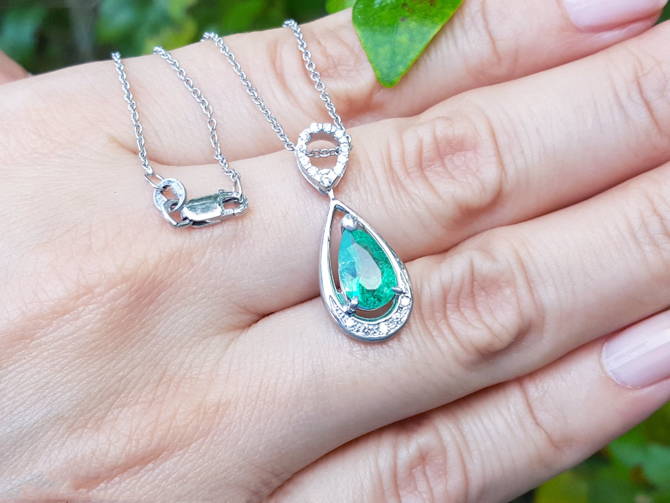 White gold emerald pendant on a hand with a blurred green background.