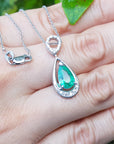 White gold emerald pendant on a hand with a blurred green background.