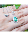 White gold emerald pendant on a hand with a blurred green background.