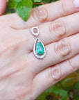 White gold necklace with a pear cut emerald held on a hand against a natural background.