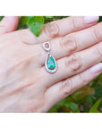 White gold necklace with a pear cut emerald held on a hand against a natural background.