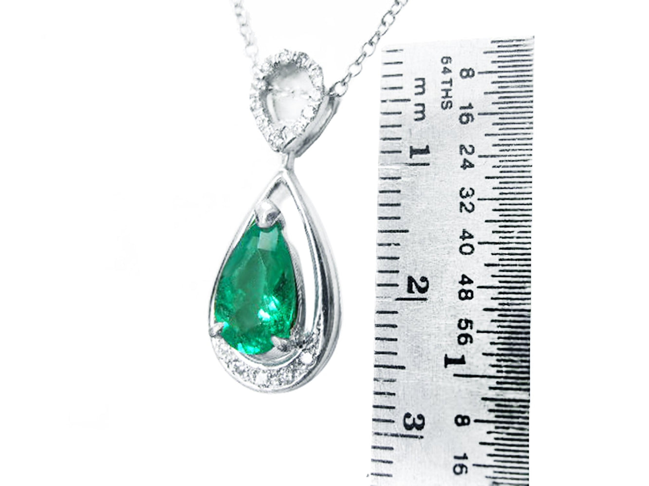 Teardrop-shaped emerald pendant with white gold chain on a ruler for scale