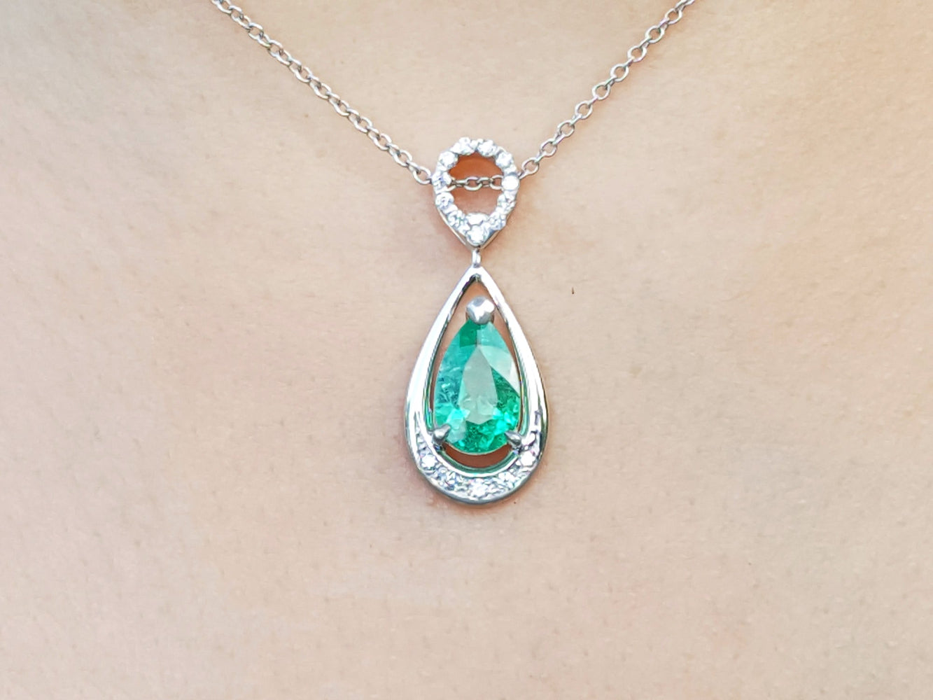 Teardrop-shaped emerald pendant on a chain against a beige skin background.