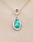 Teardrop-shaped emerald pendant on a chain against a beige skin background.