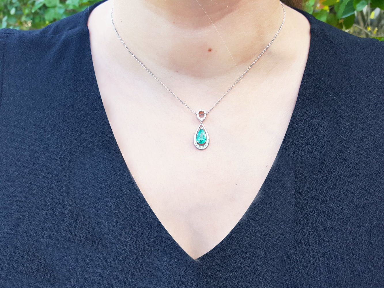 Necklace with a natural emerald pendant on a person wearing a black top.