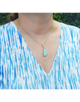 A woman wearing a blue and white patterned top with a gold necklace and natural opal pendant.