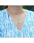 Pear-shaped Australian opal pendant with halo diamonds on an 18K gold chain, worn on a woman.