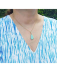 Pear-shaped Australian opal pendant with halo diamonds on an 18K gold chain, worn on a woman.