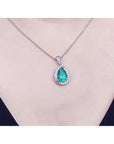 Emerald green teardrop pendant on a white gold chain against a neutral background