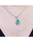 Pear-shaped natural emerald pendant with diamond halo on a 14K white gold chain, worn on a person.