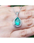 Green teardrop emerald pendant with white gold chain on a hand.