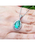 Emerald green teardrop pendant on a white gold chain held in a hand.