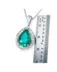 Pendant with pear cut emerald and white gold chain next to a ruler for size reference on a white background
