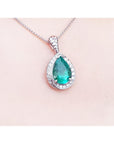 Emerald green teardrop pendant with diamonds on a skin background