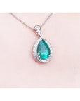 Pear-shaped natural emerald pendant with diamond halo, set in 14K white gold on a delicate chain.