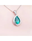 Pear-shaped natural emerald pendant with diamond halo, set in 14K white gold on a delicate chain.