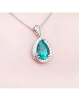 Pear-shaped natural emerald pendant with diamond halo, set in 14K white gold on a delicate chain.