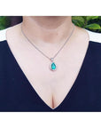 Pear-shaped natural emerald pendant with diamond halo on a 14K white gold chain, worn on a woman's neck.