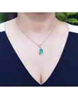 Pear-shaped natural emerald pendant with diamond halo on a 14K white gold chain, worn on a woman's neck.