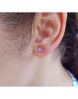Close-up of an ear wearing a pink cabochon sapphire earring with blurred background.