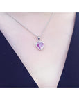 Pink sapphire heart pendant with diamond halo on an 18K white gold chain, worn on a person.