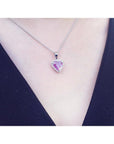 Pink sapphire heart pendant with diamond halo on an 18K white gold chain, worn on a person.