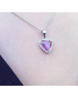 Heart-cut pink sapphire pendant with diamond halo on an 18K white gold chain, worn on a person.