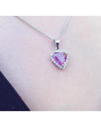Heart-cut pink sapphire pendant with diamond halo on an 18K white gold chain, worn on a person.