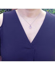 Pink sapphire heart pendant with halo diamonds on an 18K white gold chain, worn on a woman's neck.