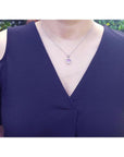 Pink sapphire heart pendant with halo diamonds on an 18K white gold chain, worn on a woman's neck.