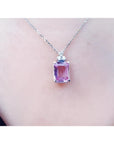 Emerald cut natural pink sapphire necklace in 14K white gold, worn on a person.