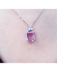 Emerald cut natural pink sapphire necklace in 14K white gold, worn on a person.