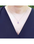 Emerald cut natural pink sapphire necklace in 14K white gold, worn on a person.