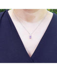Emerald cut natural pink sapphire necklace in 14K white gold, worn on a person.