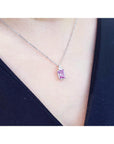 Necklace with a pink sapphire gemstone pendant on a person wearing a black top.