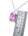 Necklace with a pink emerald cut sapphire gemstone next to a ruler for size reference on a white background