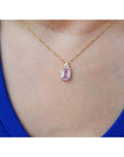 Gold necklace with a natural pink sapphire pendant worn by a person in a blue top.