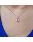 Gold necklace with a natural pink sapphire pendant worn by a person in a blue top.