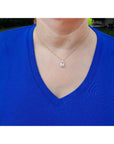 Person wearing a blue shirt with a gold necklace featuring a pink sapphire pendant.