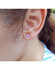 Close-up of a woman wearing a pink sapphire stud earring with blurred background.